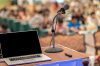 Microphone and laptop on table in front of conference audience.